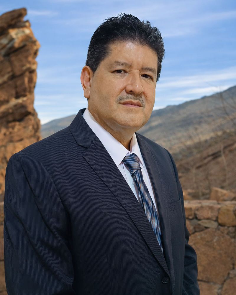 Martin Nuñez in a suit posing confidently against a rocky outdoor backdrop with a clear sky.