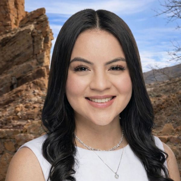 Brianna Cervantes with long hair, wearing a necklace, in front of a rocky desert landscape under a clear blue sky.