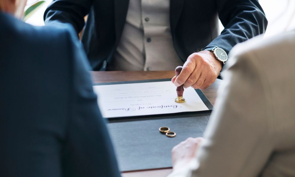 Official sealing of divorce certificate in presence of couple and document with wedding rings on table.