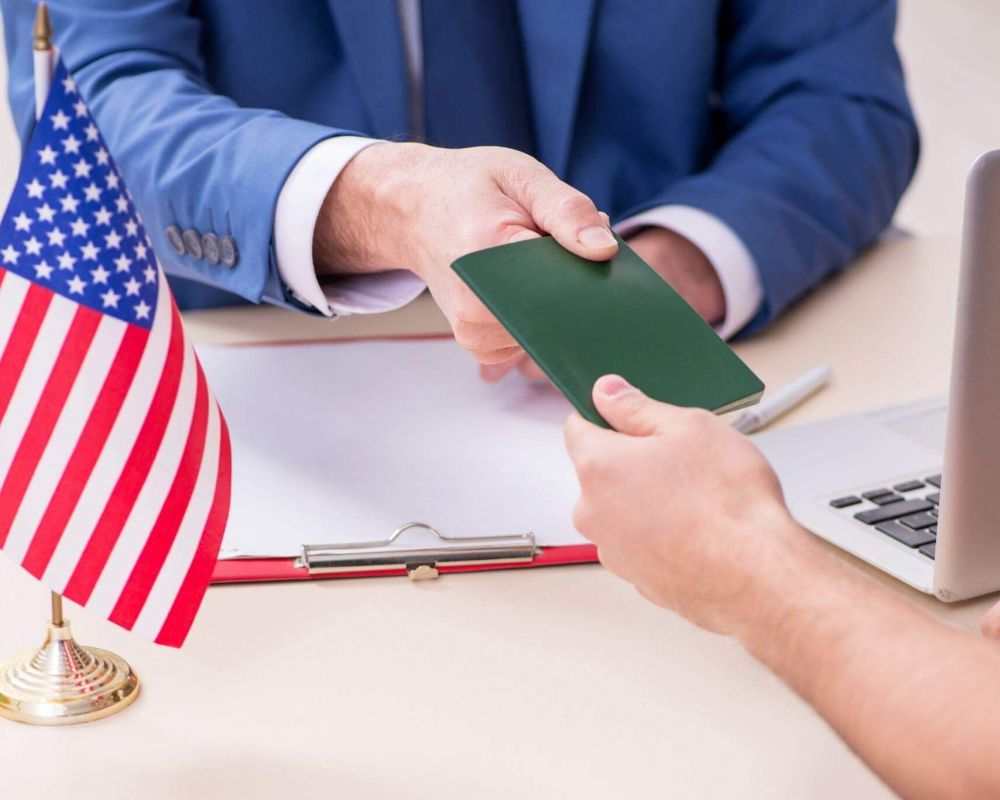 a man in a blue suit is holding a green card, there's an american flag on the table