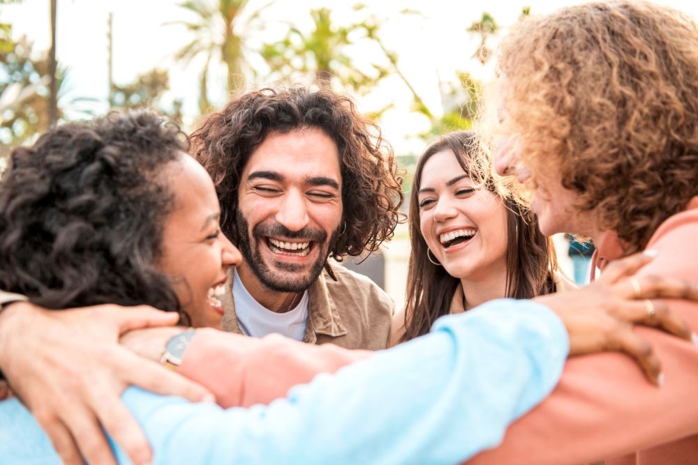 A diverse group of friends joyfully embracing outdoors, laughing and enjoying a sunny day together.