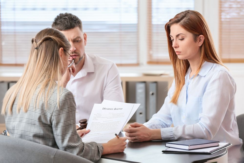 Three people discussing a divorce decree in an office setting, with a lawyer present.