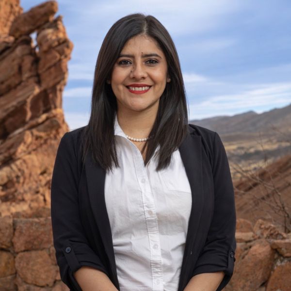 Smiling woman in business attire standing outdoors with rocky landscape background.