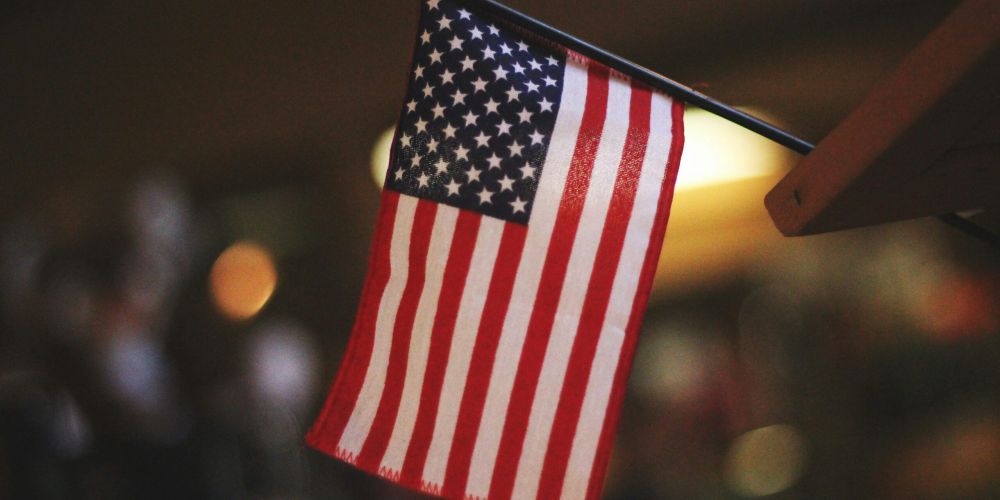 Small American flag on a stick, hanging indoors with blurred background lights