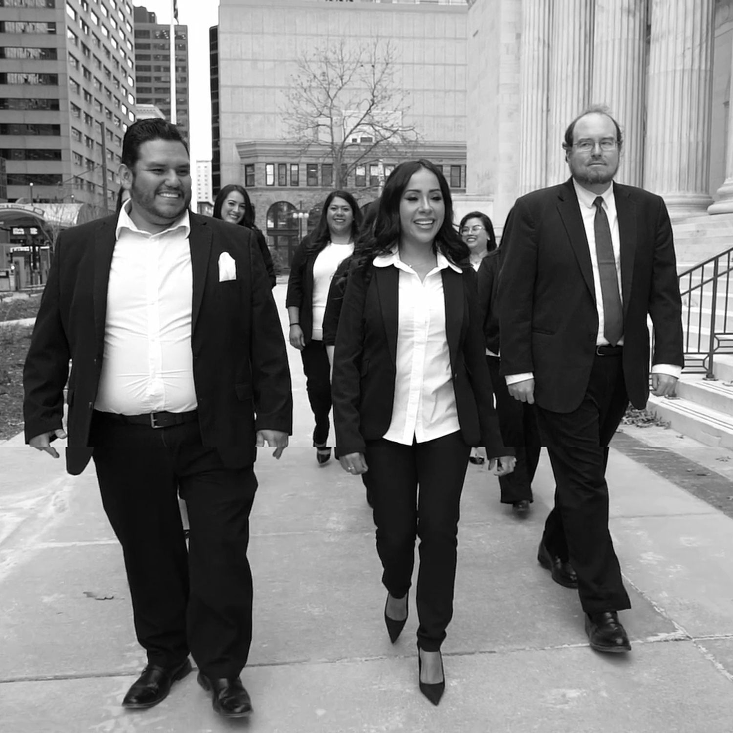 Business team walking confidently in city street, wearing formal attire and smiling.