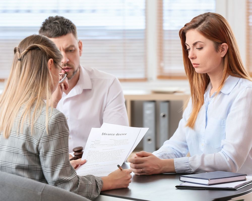 Three people discussing a divorce decree in an office setting, with a lawyer present.