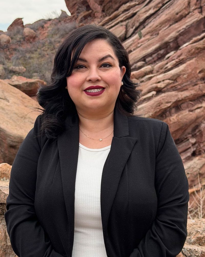Lenny Alfaro in black blazer smiling in front of rocky landscape.