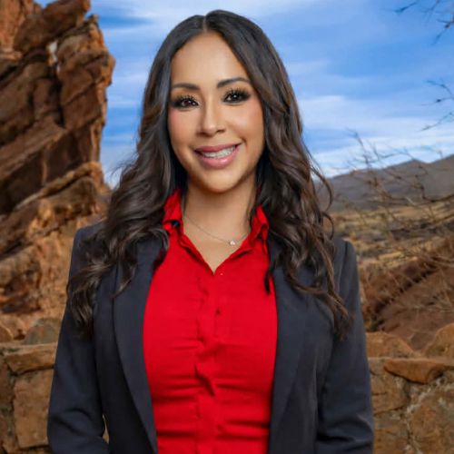 Smiling woman in a red shirt and black blazer with rocky landscape in the background.