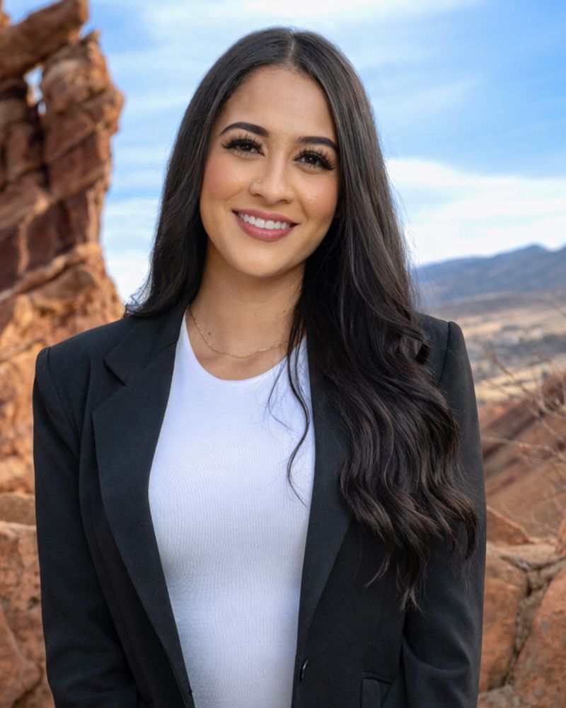 Smiling woman in black blazer outdoors with rocky landscape in the background.