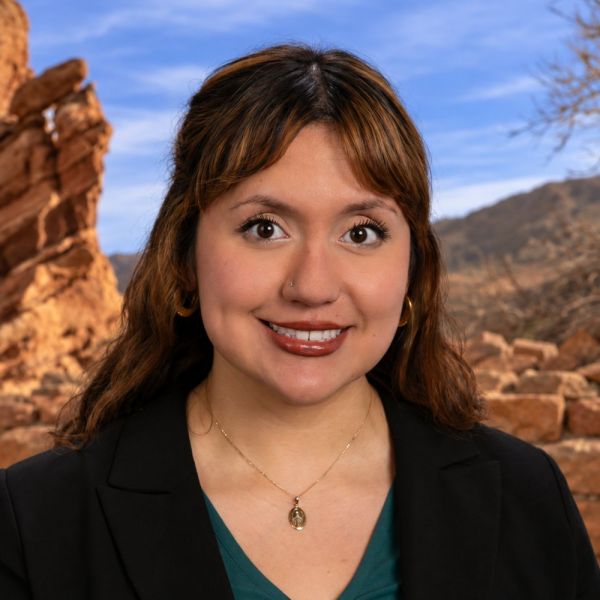 Vianey Almaguer in black blazer smiling outdoors with rocky landscape background.