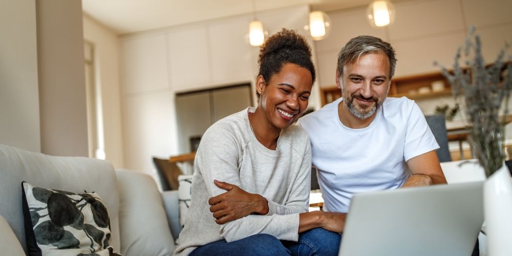 Smiling couple on a couch enjoying laptop screen in cozy living room setting.