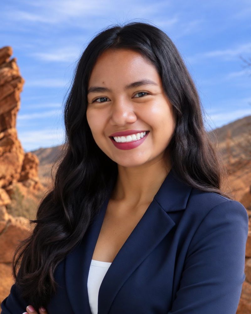 Yaquelin Rivera in navy blazer smiling outdoors with rocky landscape background.