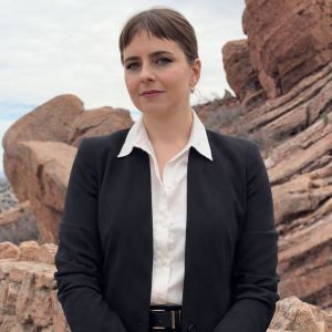 Carolyn Bayens in black suit standing confidently against rocky landscape background.