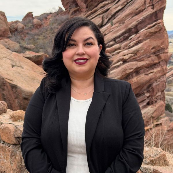 Lenny Alfaro in black blazer smiling in front of rocky landscape.