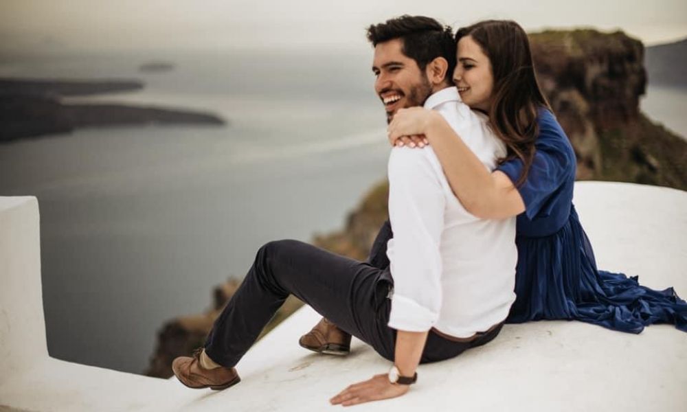 Couple enjoying a romantic moment on a seaside cliff with a scenic ocean view in the background.