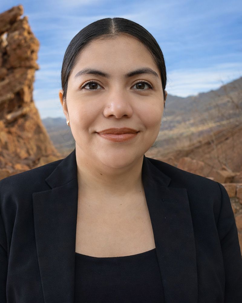 Leidy in black blazer smiling outdoors with rocky landscape background.