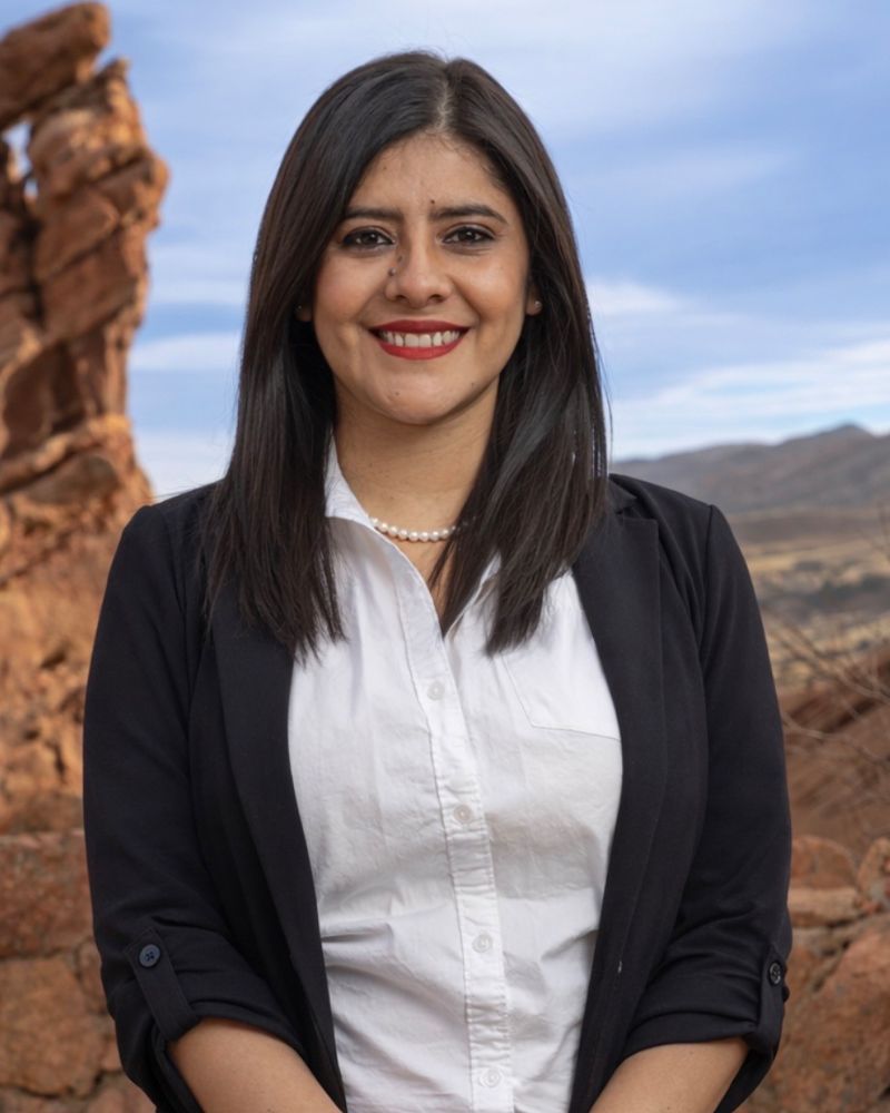 Smiling woman in business attire standing outdoors with rocky landscape background.