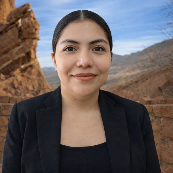 Leidy in black blazer smiling outdoors with rocky landscape background.