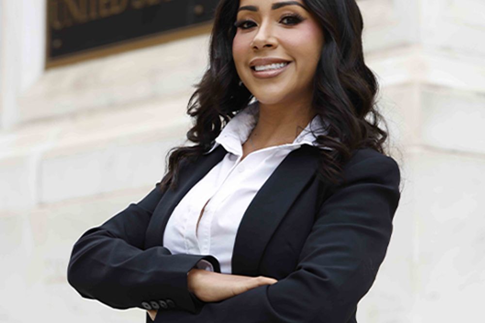 Confident professional woman in a suit standing in front of a courthouse with arms crossed, smiling.