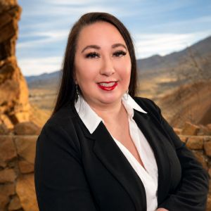 Melina Somoza in business attire smiles outdoors with scenic mountain background.