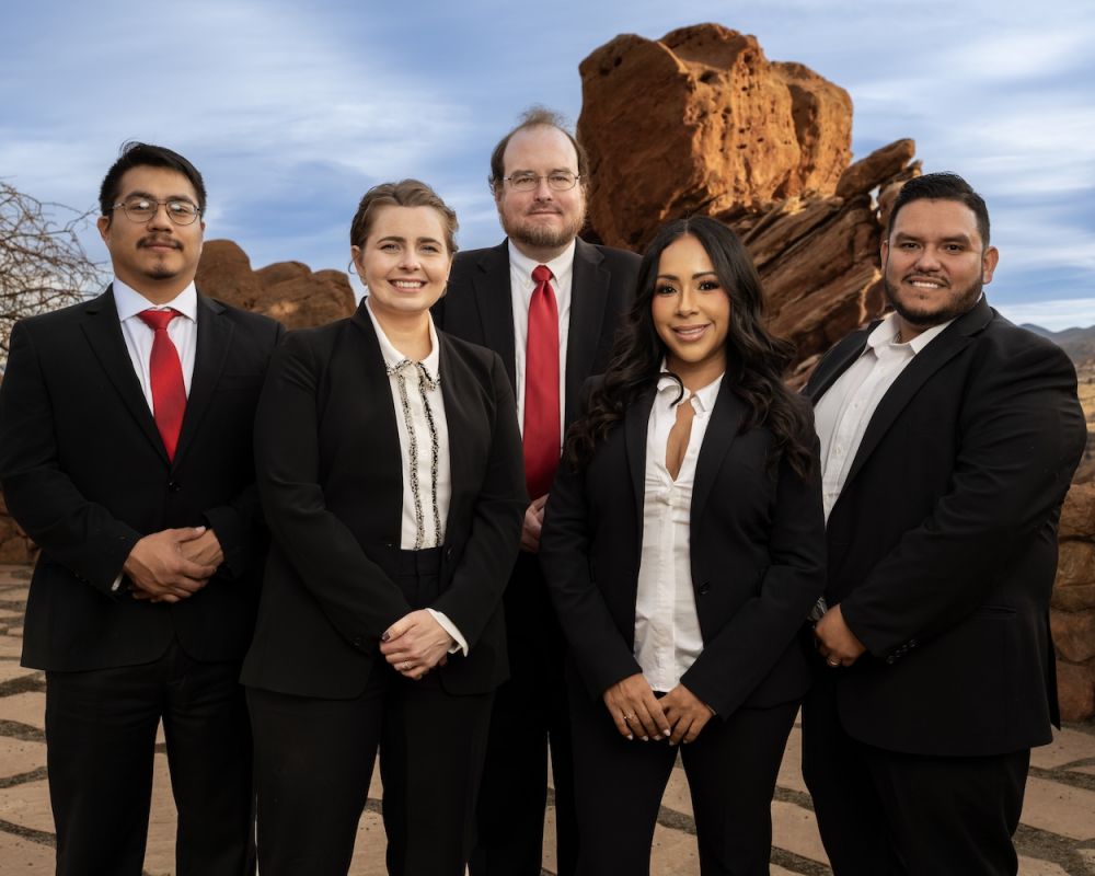 Business team in suits posing outdoors with rocky landscape background.