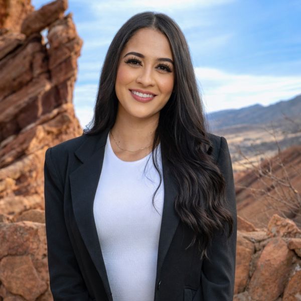 Smiling woman in black blazer outdoors with rocky landscape in the background.