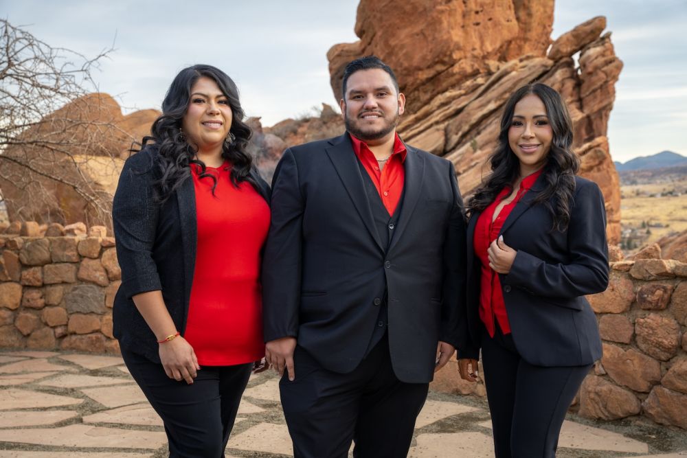 Three professionals in red and black suits posing outdoors with rocky landscape background.
