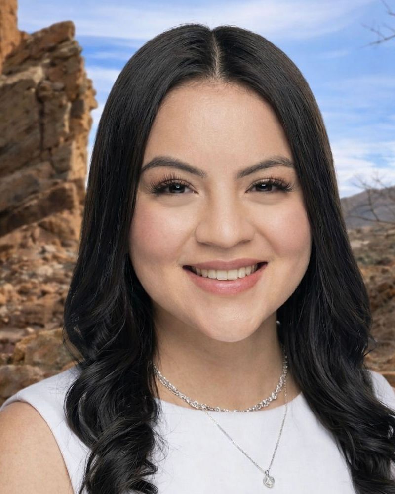 Brianna Cervantes with long hair, wearing a necklace, in front of a rocky desert landscape under a clear blue sky.
