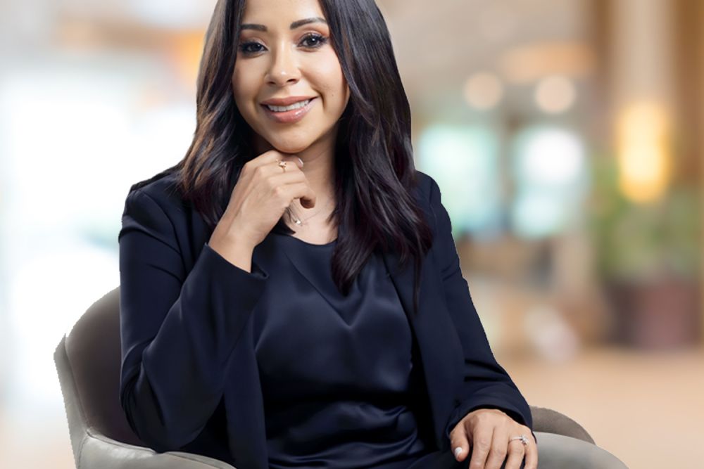 Smiling woman in business attire seated in modern office setting.