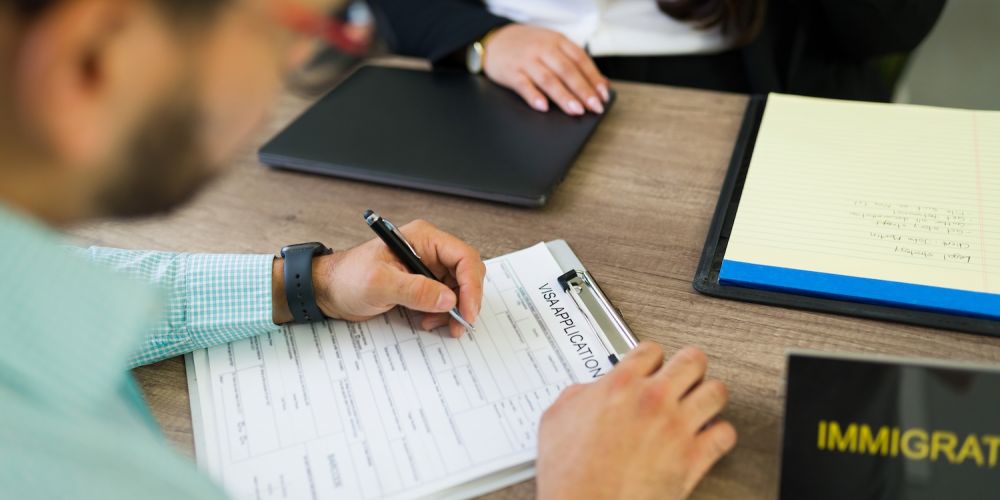 Person filling out visa application form at immigration office counter.