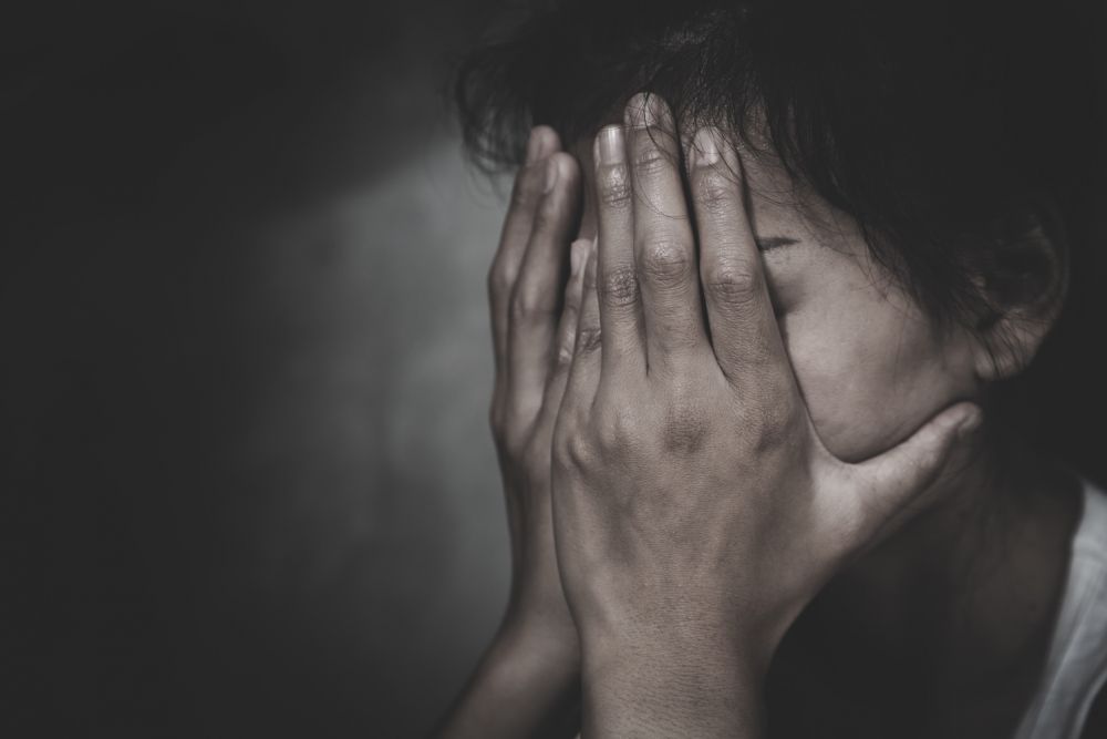 Person covering face with hands, expressing stress or anxiety in a dark, moody setting.