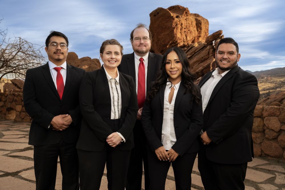Business team in suits posing outdoors with rocky landscape background.