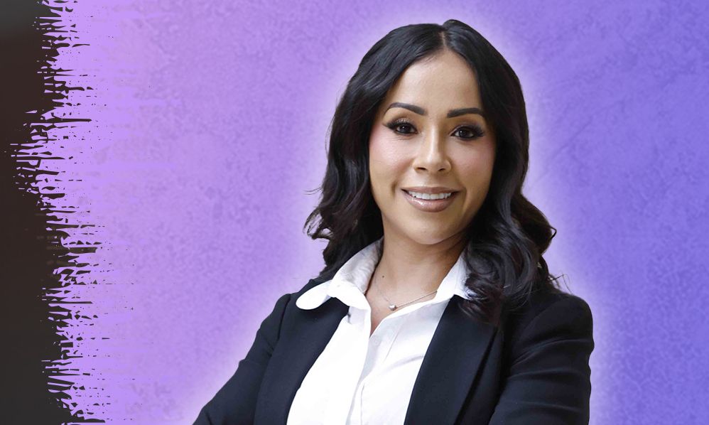 Maria Monclova in a suit on a purple background, confident and professional.