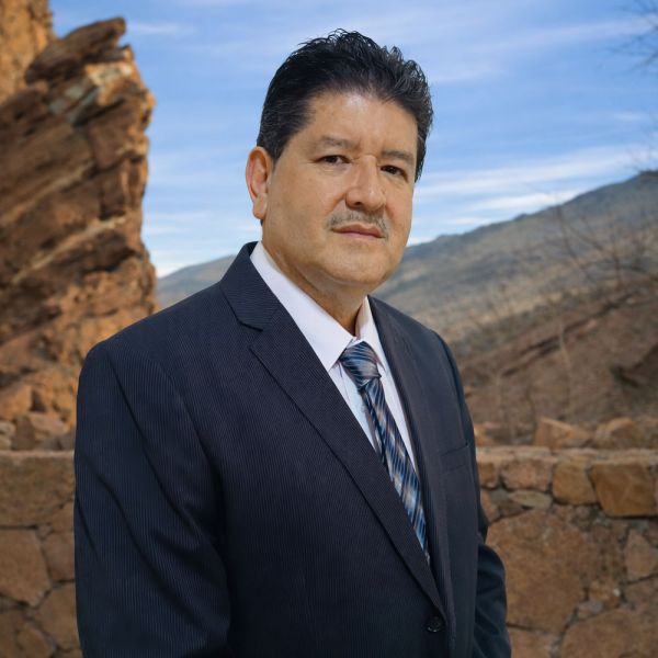 Martin Nuñez in a suit posing confidently against a rocky outdoor backdrop with a clear sky.