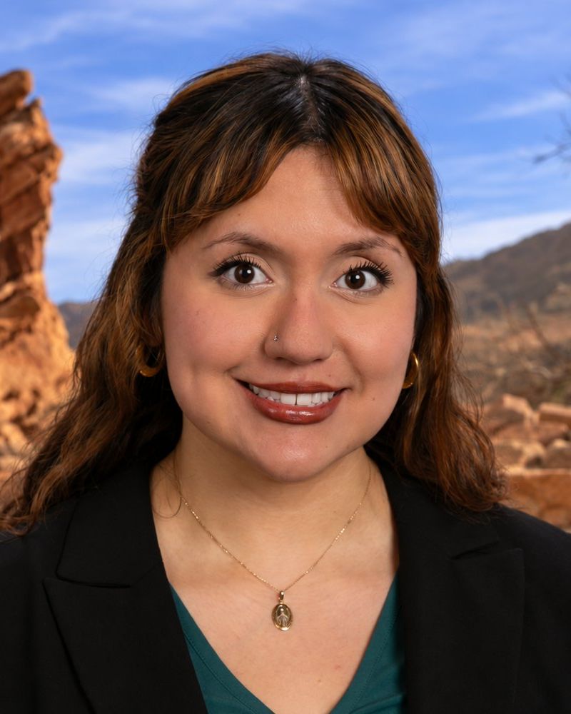 Vianey Almaguer in black blazer smiling outdoors with rocky landscape background.