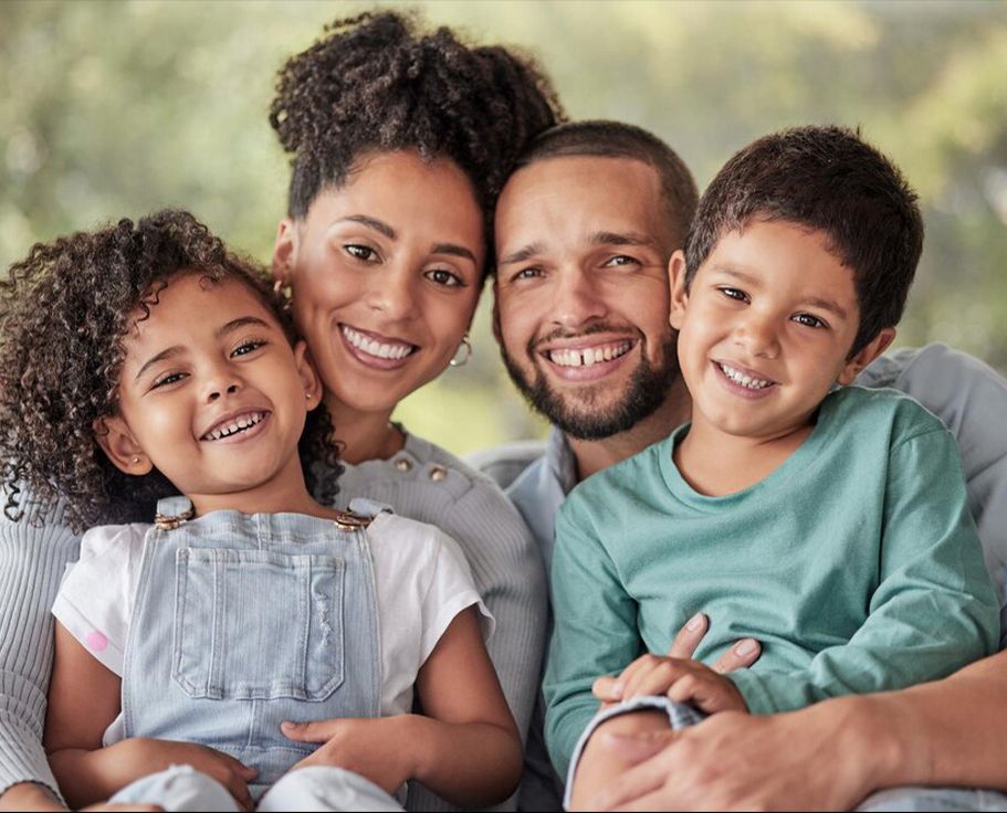 Happy family smiling together outdoors in a park setting, expressing joy and togetherness on a sunny day.